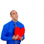 Man looking upwards, holding red heart to chest daydreaming of women in love